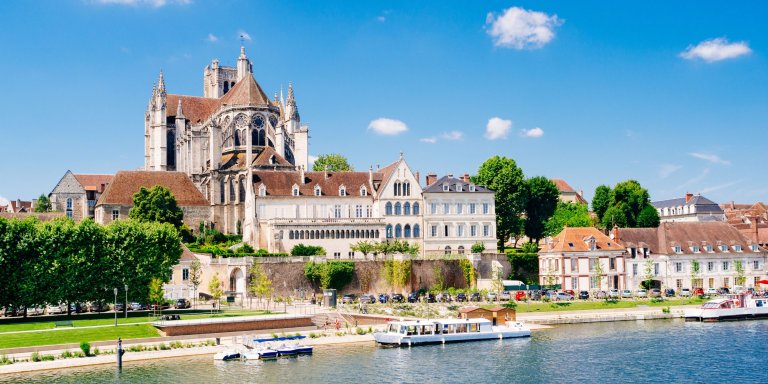 Auxerre Cathedral in France with the Yonne River flowing beside it. A boat can be seen on the river.